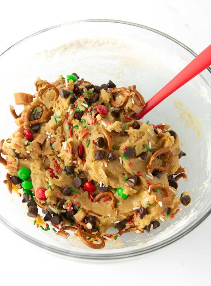 mixed bowl of christmas cookie dough with pretzels, holiday m&m's, chocolate chips, pretzels, and caramel