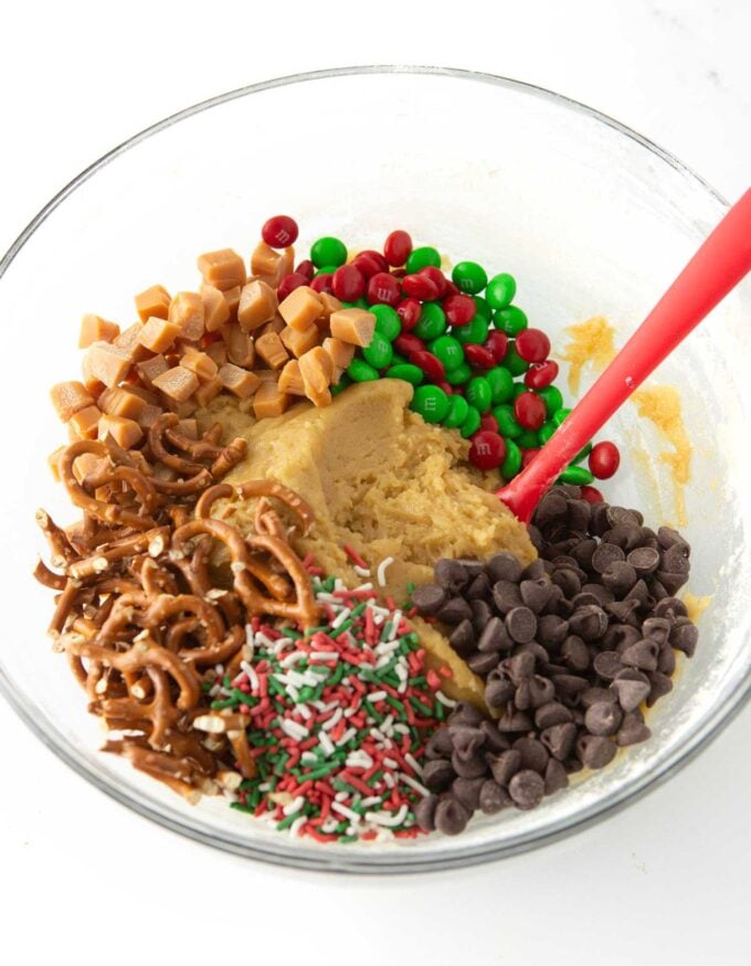 bowl of christmas cookie dough with pretzels, holiday m&m's, chocolate chips, pretzels, and caramel