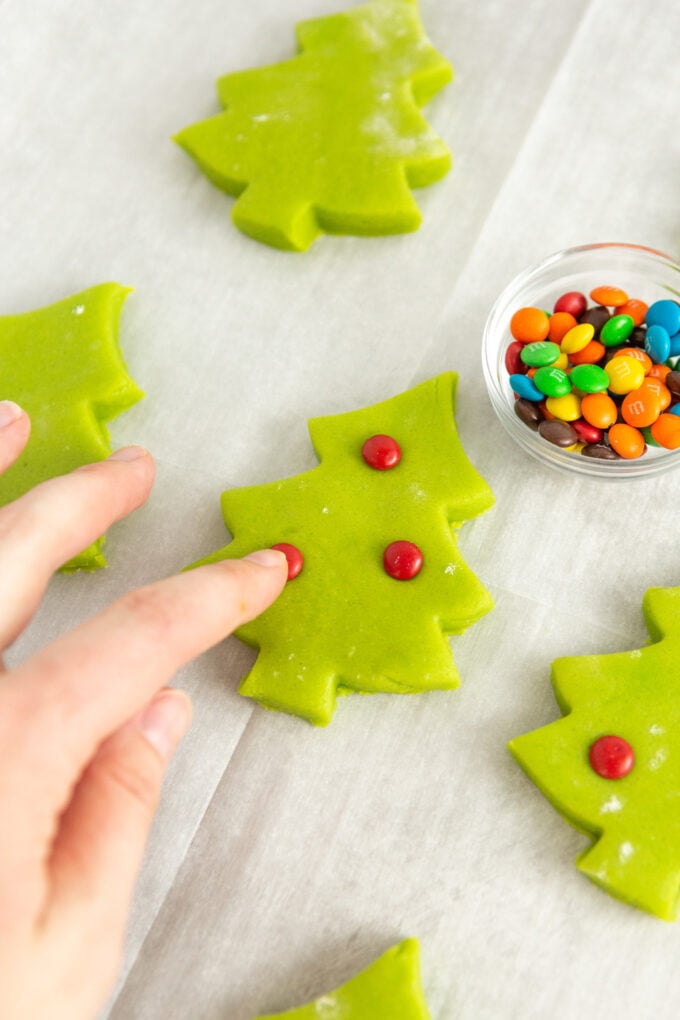 finger pressing mini red M&M candy into green christmas tree dough