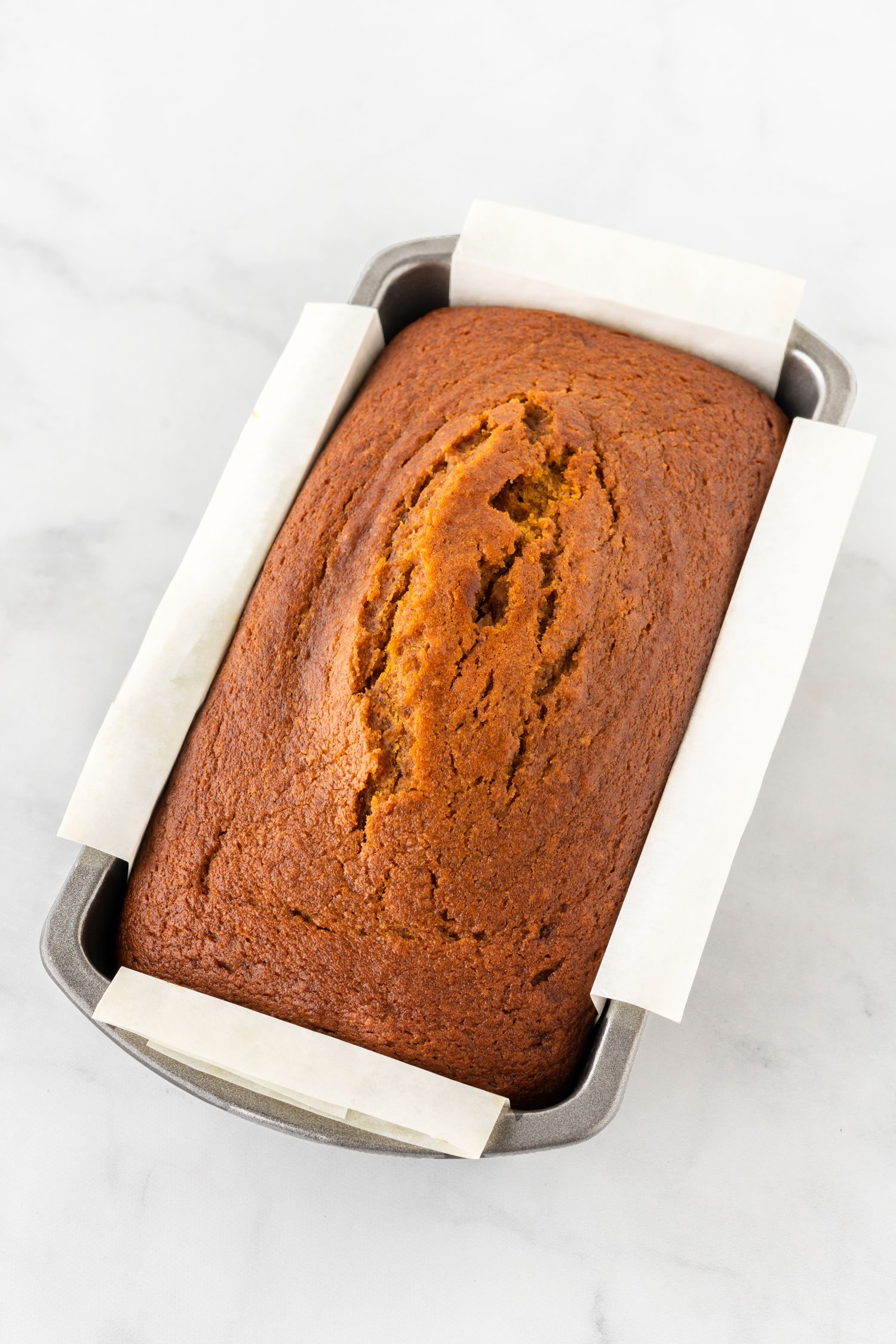 baked pumpkin bread in metal loaf pan with parchment sling