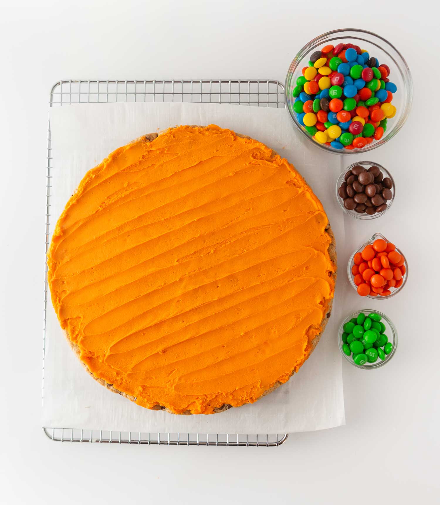 orange cookie cake on wire rack with bowls of m&m's