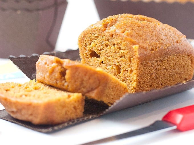 Moist pumpkin bread mini loaf pan recipe in tiny disposable loaf pans cut in slices with red knife.