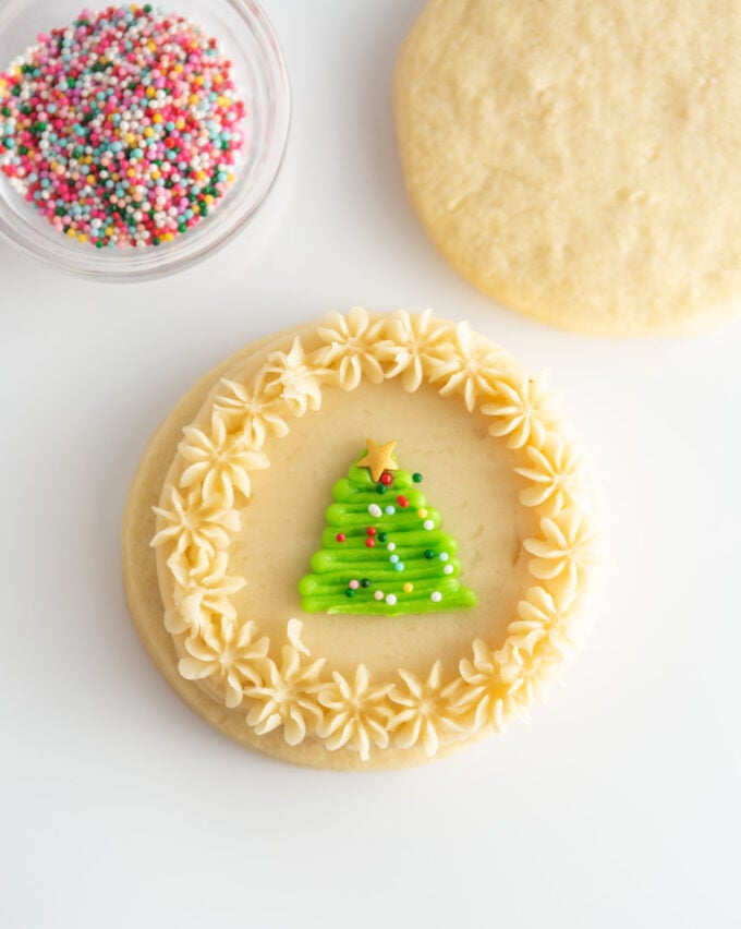 white sugar cookie decorated with green tree and sprinkles in center