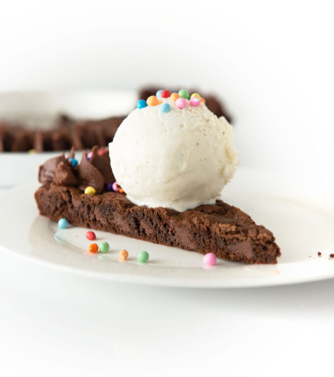 slice of triple chocolate cookie cake with scoop of vanilla ice cream and rainbow sprinkles